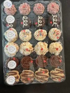Bakery case cupcakes on display trays with various frosting designs and colors